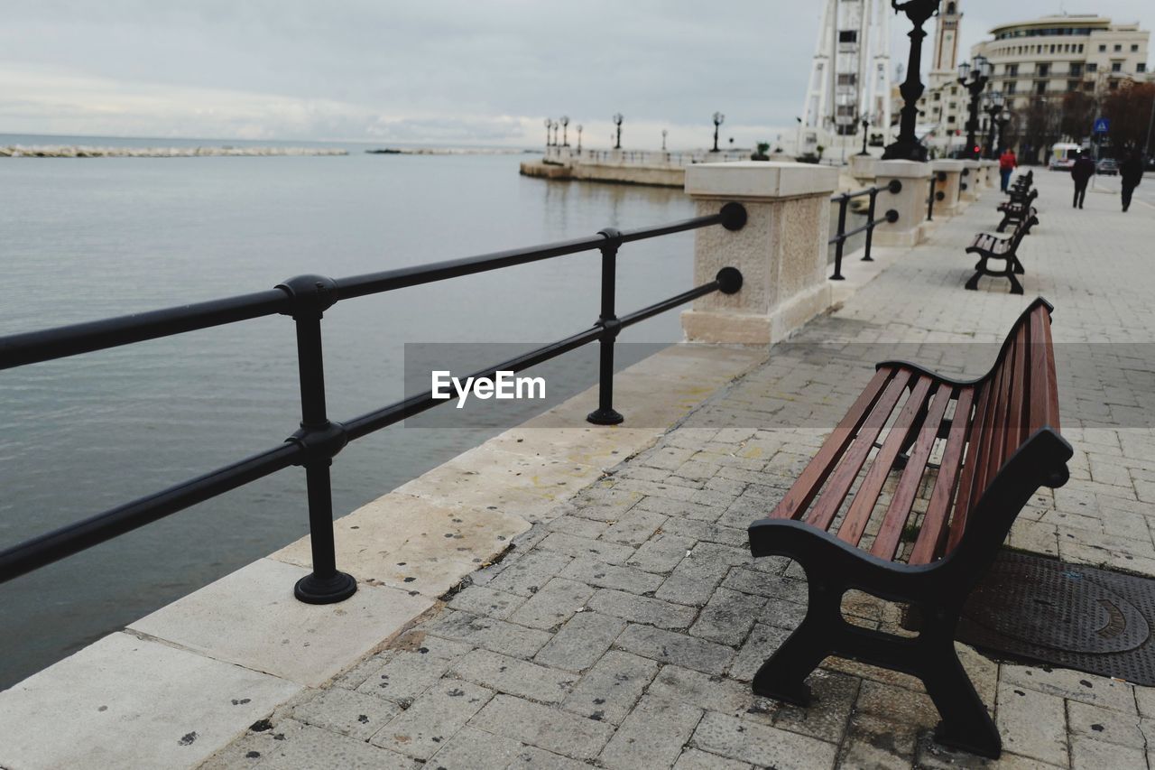 EMPTY BENCH BY PIER AGAINST SKY