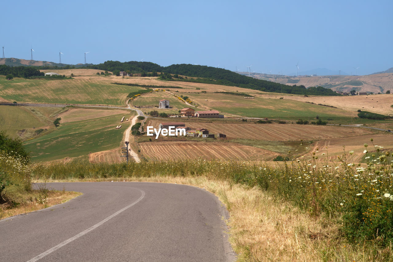 landscape, environment, road, transportation, land, rural scene, nature, scenics - nature, hill, sky, agriculture, plant, rural area, no people, beauty in nature, highway, field, tranquility, infrastructure, non-urban scene, travel, tranquil scene, clear sky, country road, day, blue, outdoors, farm, sunny, grass, plain, architecture, street, prairie, travel destinations, social issues, curve, building, remote, village, the way forward, sunlight