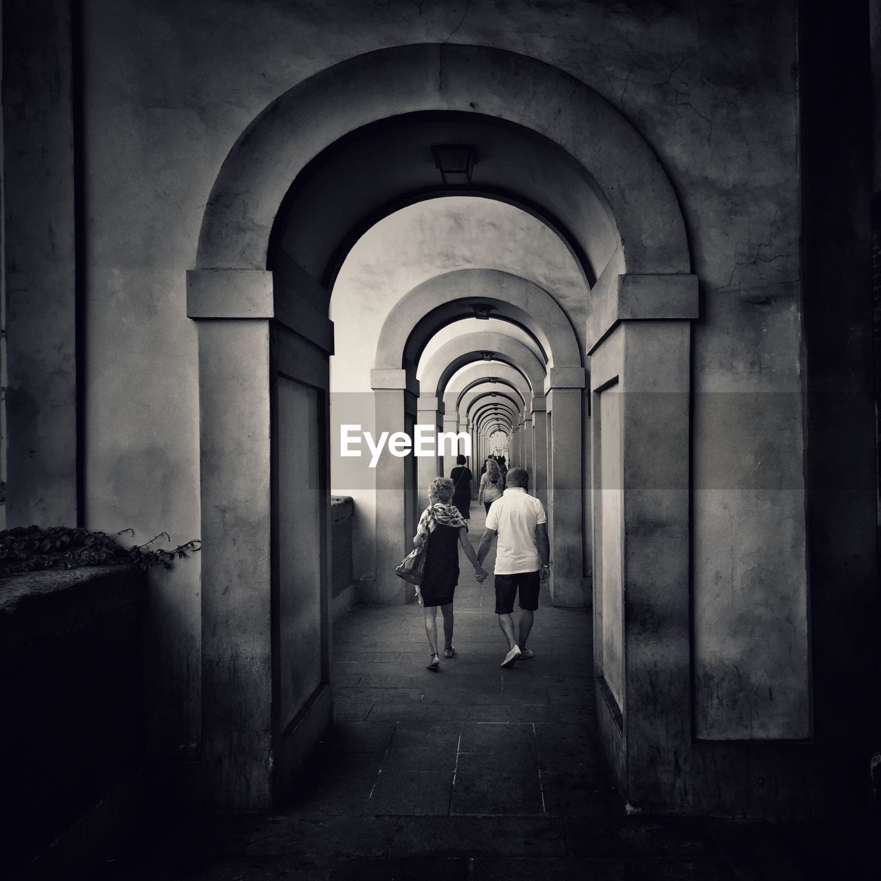 REAR VIEW OF MAN WALKING IN ARCHWAY