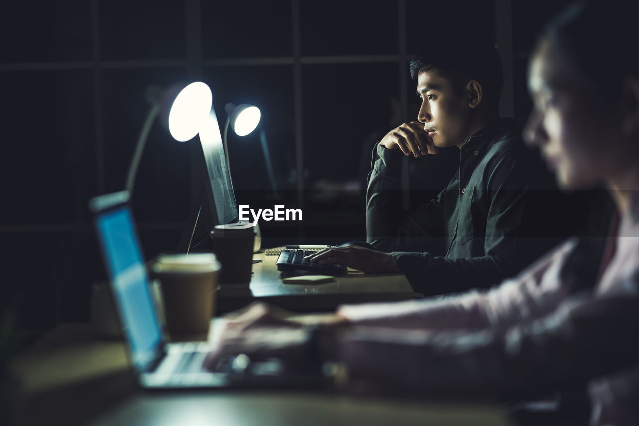 PEOPLE USING LAPTOP ON TABLE IN ILLUMINATED ROOM