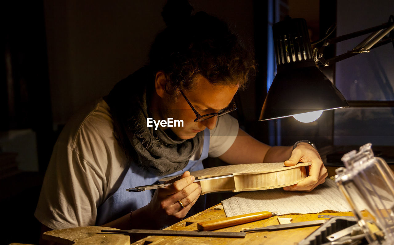 Male craftsman violin maker working on a new violin in the workshop