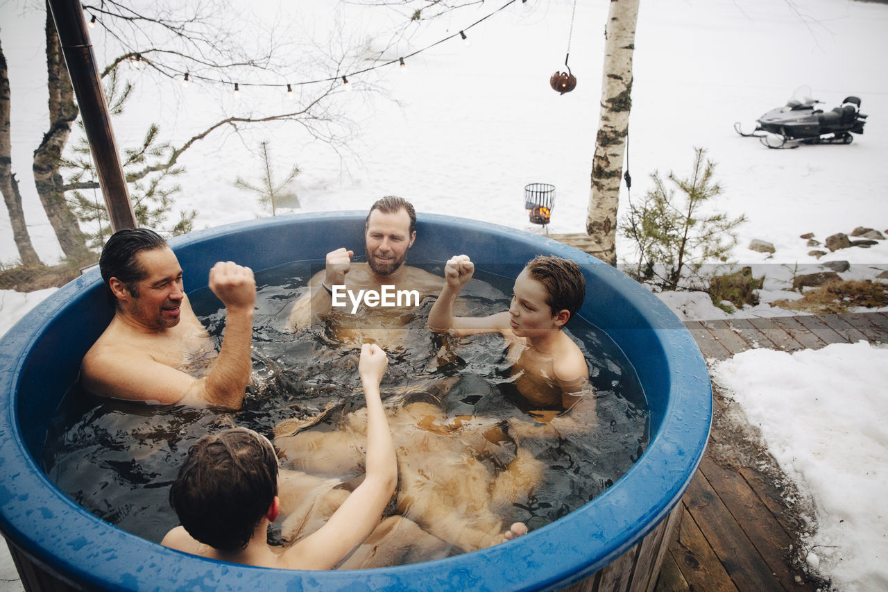 Mature men with boys gesturing fists while taking bath in hot tub