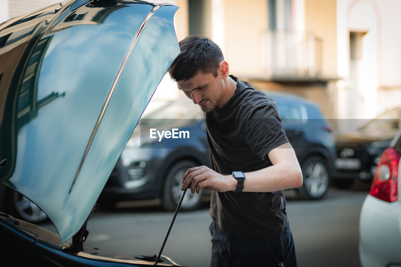 A young man checks the oil in a car engine with a dipstick.