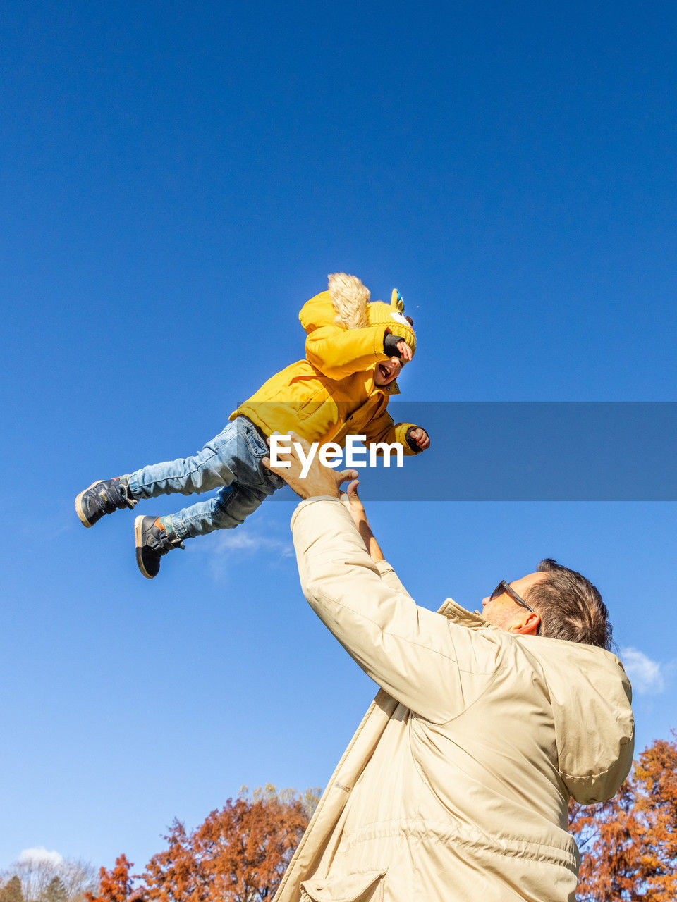 low angle view of man with arms raised standing against clear blue sky