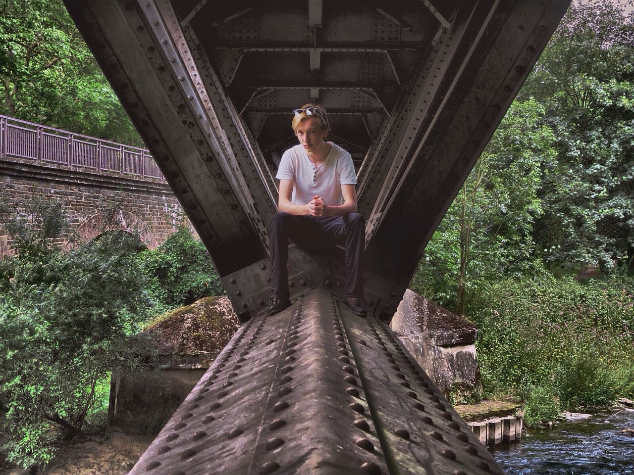 Portrait of young man sitting on bridge over river