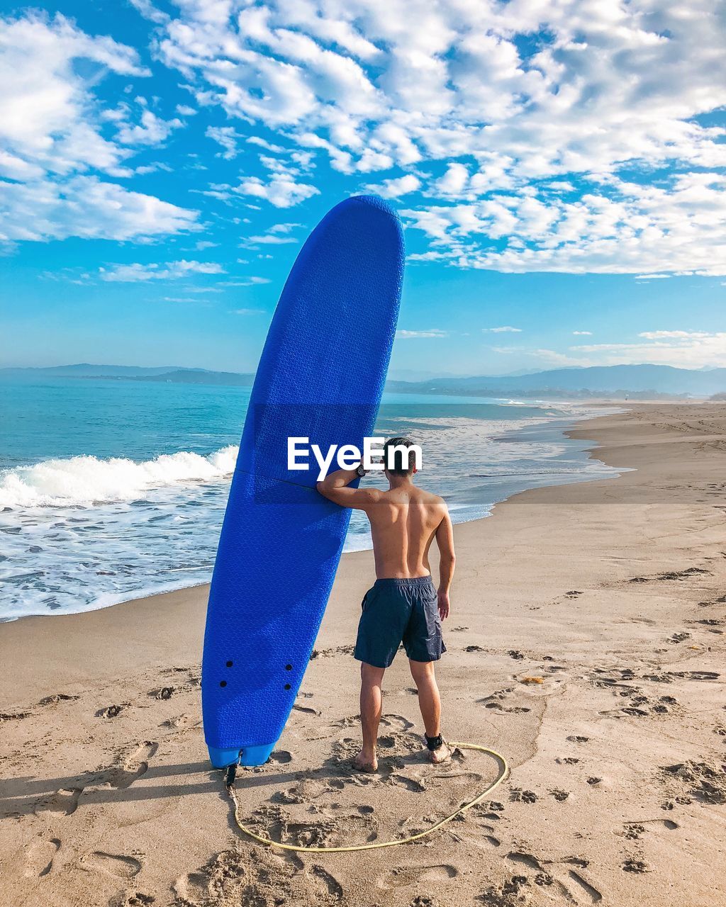 Rear view of shirtless man with surfboard standing at beach