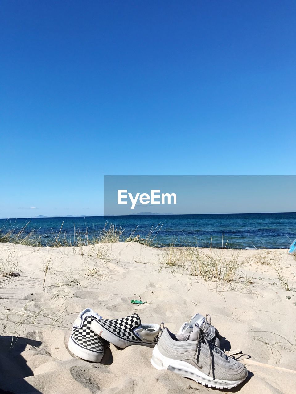 VIEW OF SHOES ON BEACH AGAINST CLEAR BLUE SKY