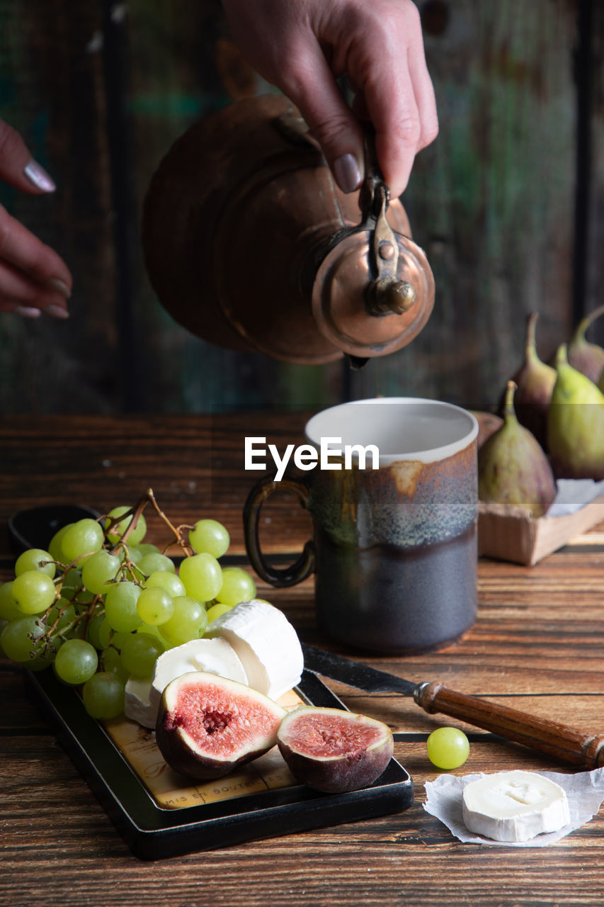 Cheese plate with goat cheese, grapes and figs, copper teapot, angle view