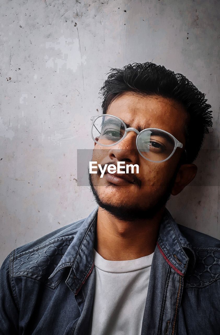 Portrait of young man wearing sunglasses against wall