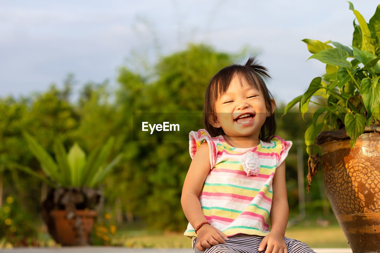 Cheerful baby girl laughing while sitting in yard