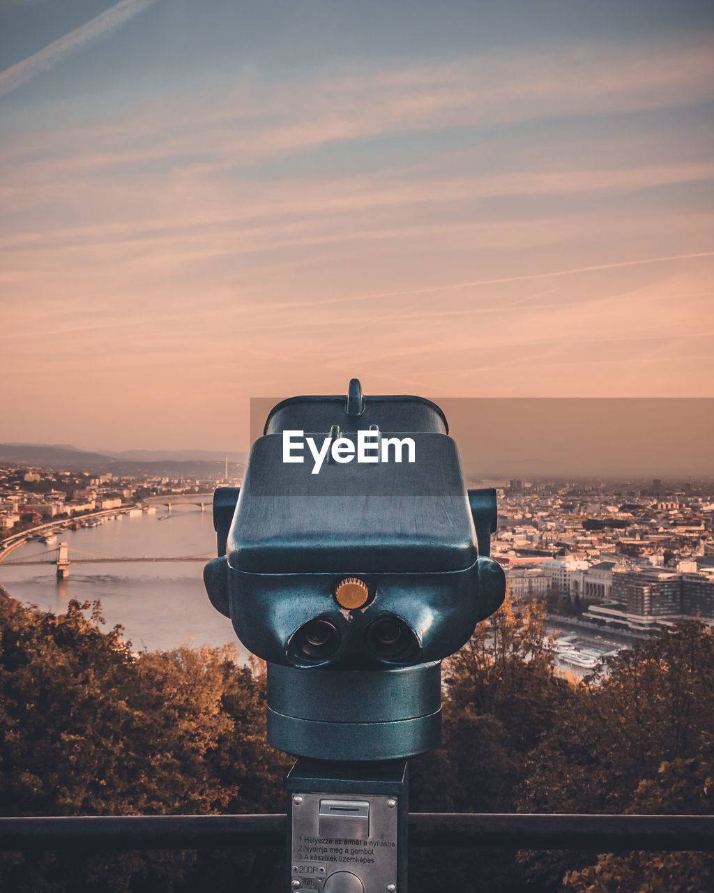 Close-up of coin-operated binoculars against cityscape during sunset