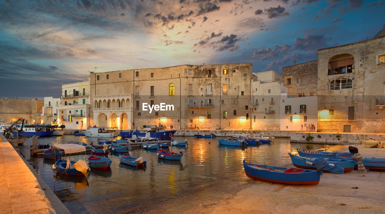 Boats moored in canal amidst buildings against sky at sunset