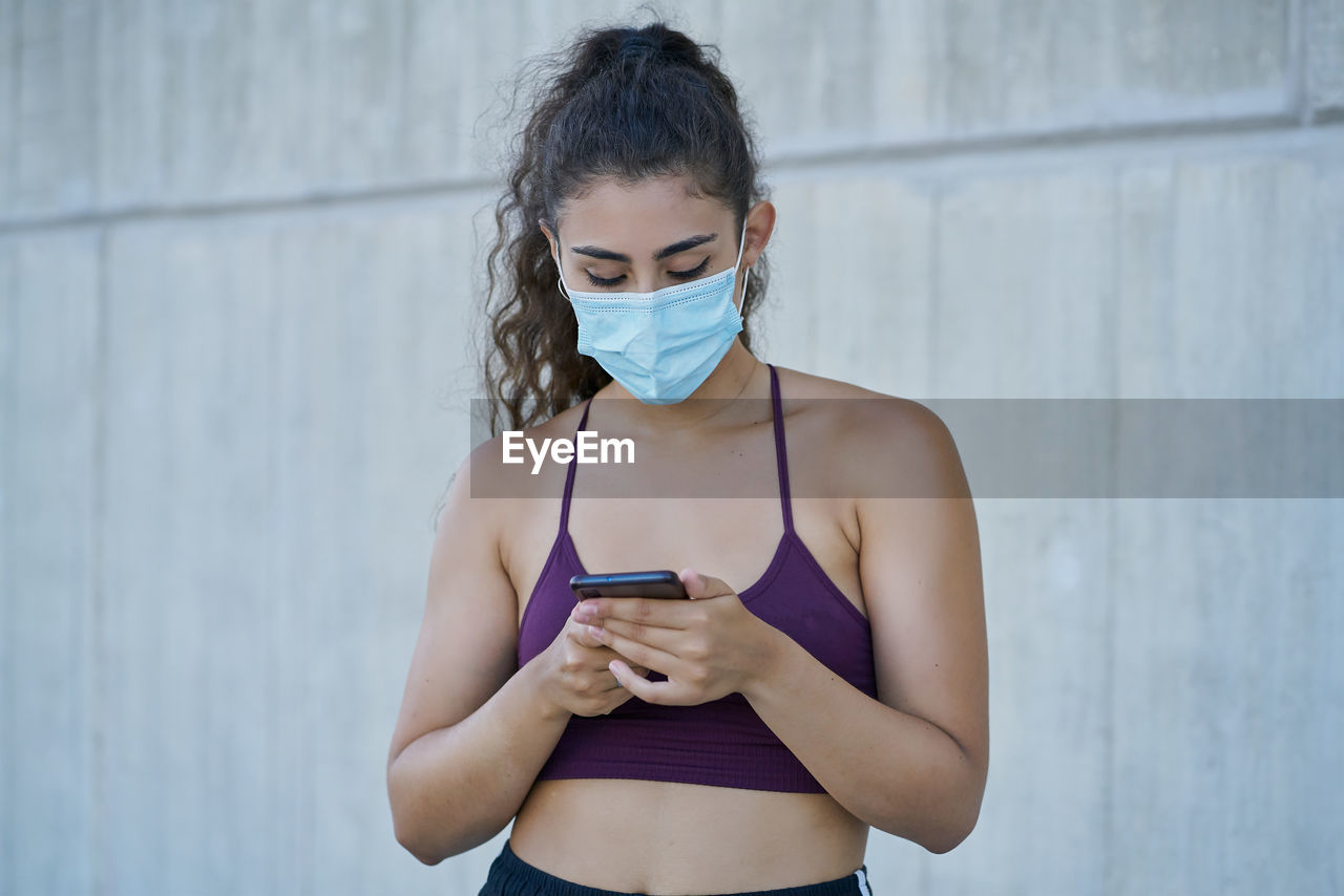 Woman in sportswear wearing a medical mask looking at a smartphone