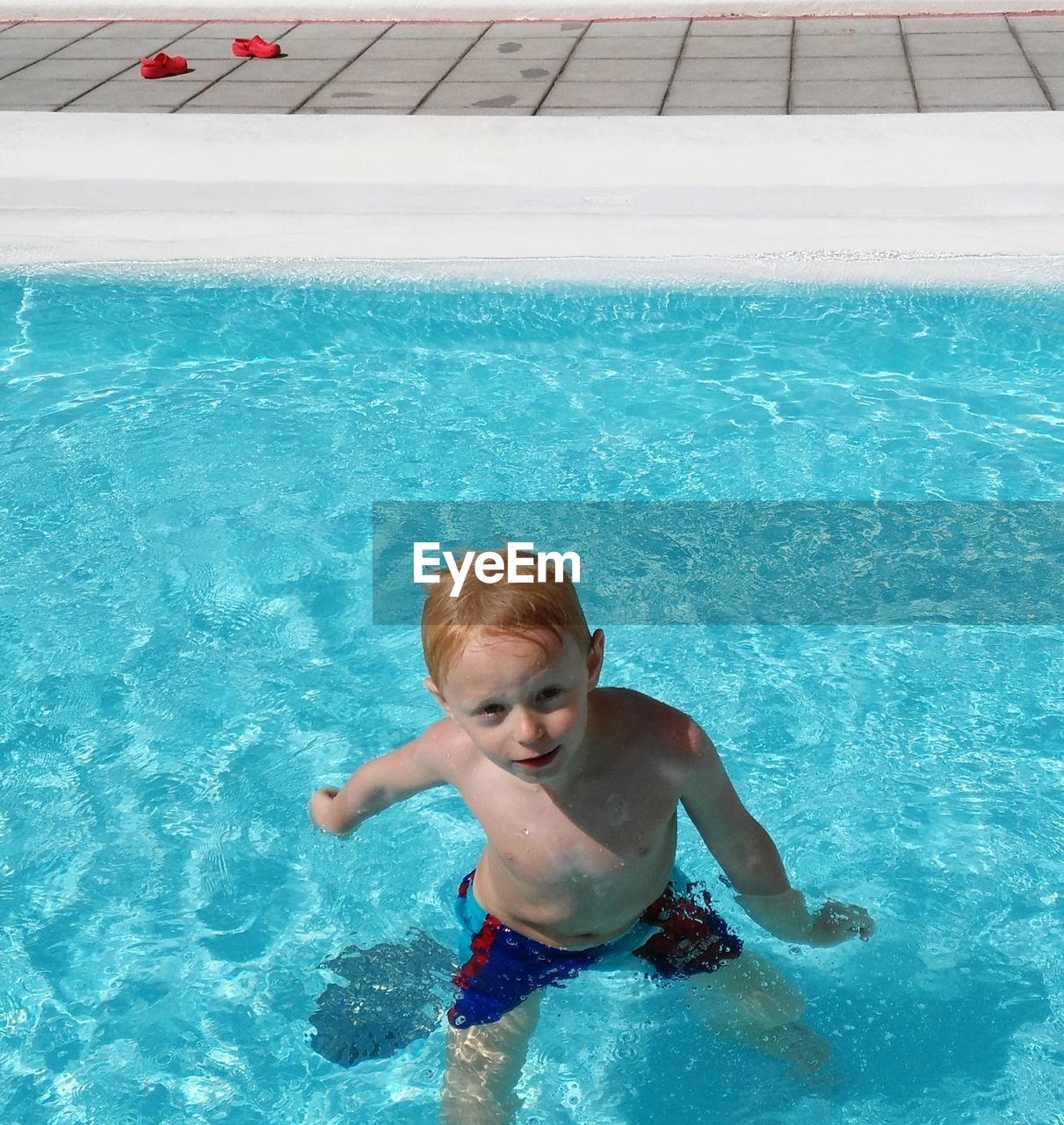 High angle portrait of boy standing in swimming pool during sunny day