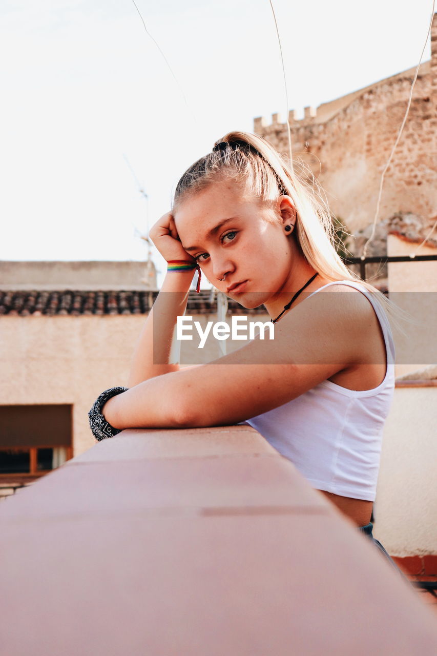 Portrait of beautiful young woman sitting against wall