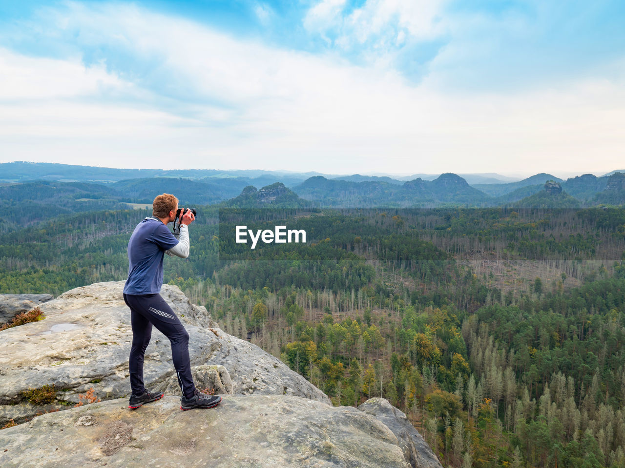 Man takes photo of landscape. photographer with eye at viewfinder of camera on stay on cliff