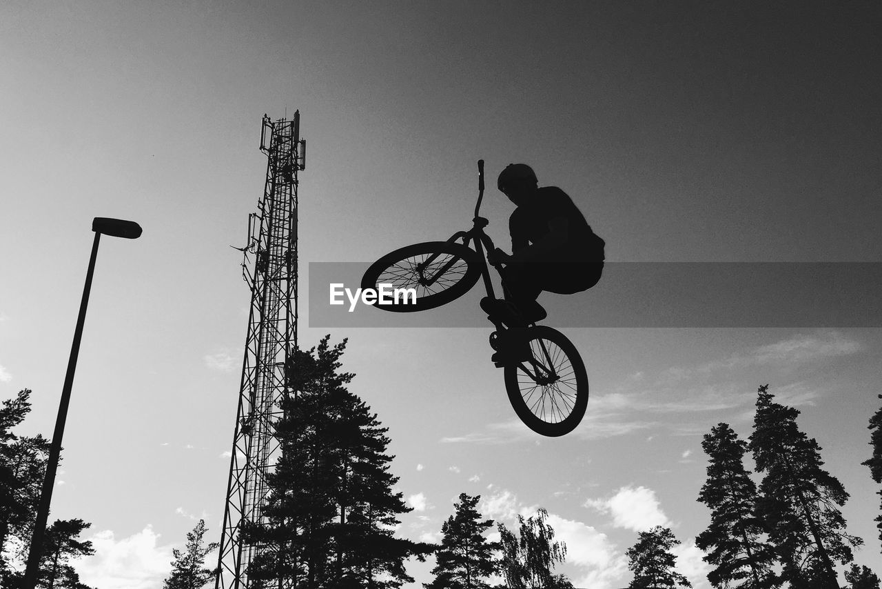 Low angle view of silhouette man jumping with bicycle against sky