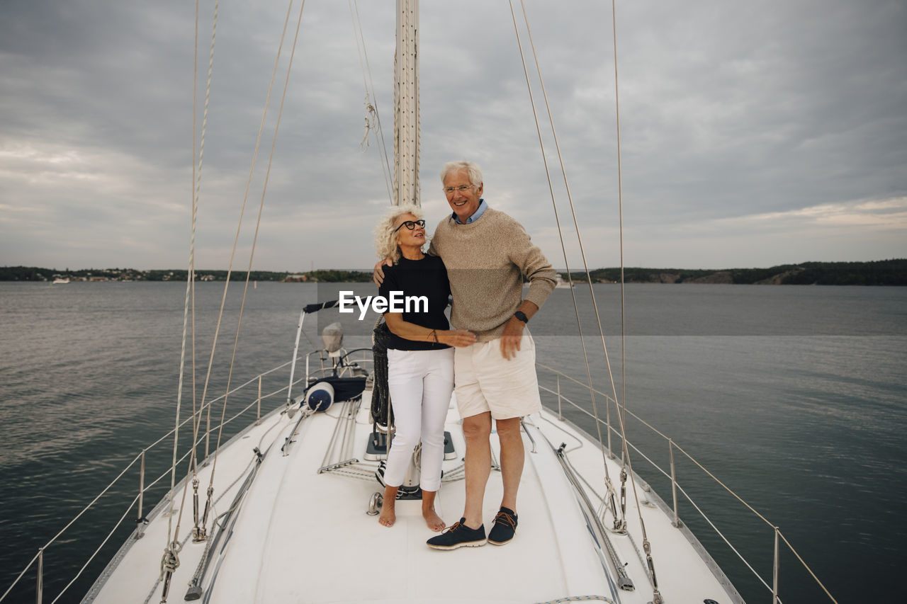 Senior woman looking at man while standing on boat against sky during sunset