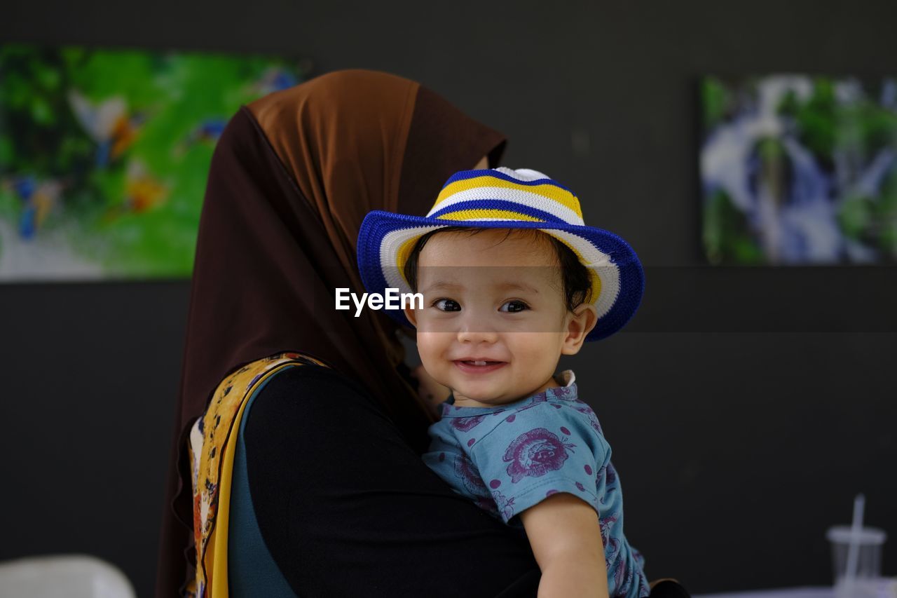 Side view of mother carrying cute daughter while standing against wall