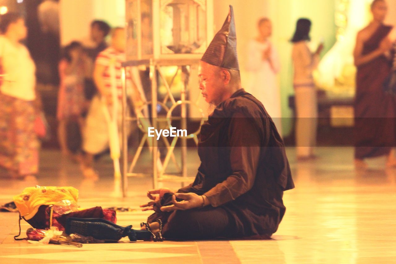 Side view of monk meditating while sitting on floor