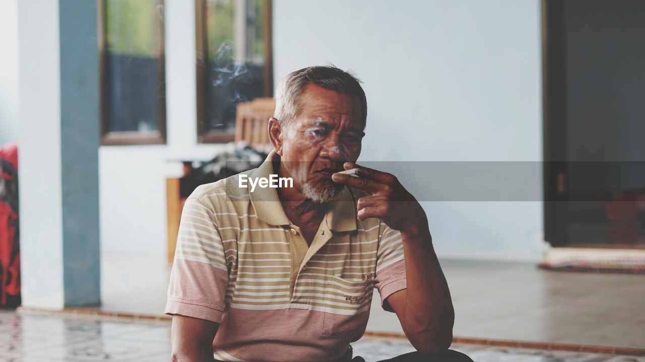 PORTRAIT OF MAN LOOKING AWAY WHILE STANDING ON WINDOW