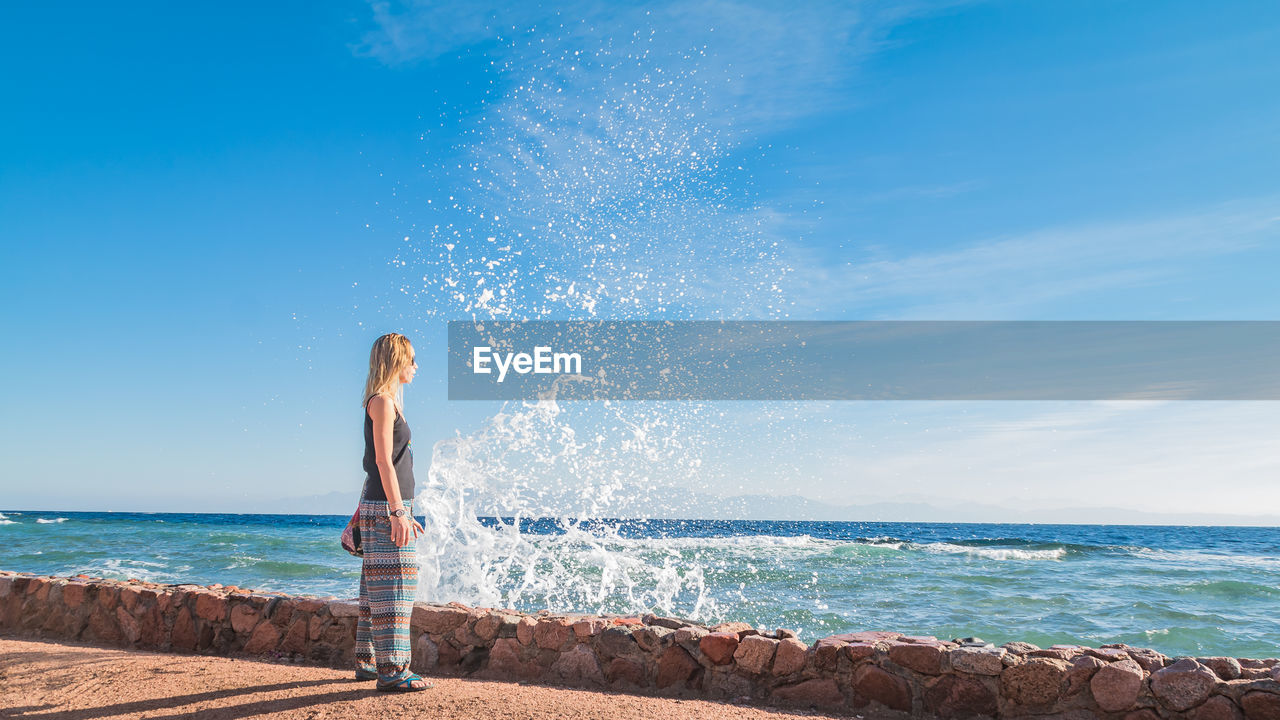 Woman standing at beach against blue sky