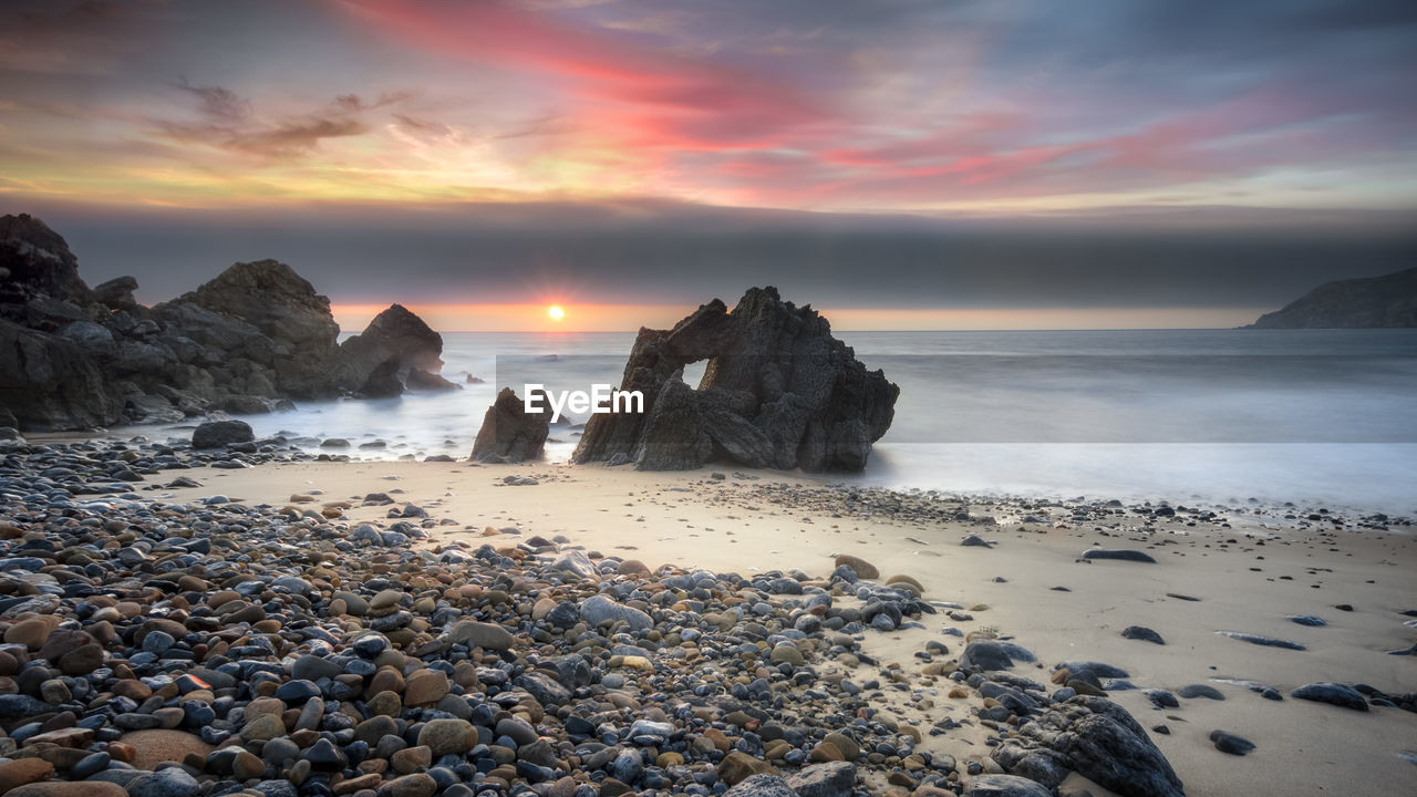 SCENIC VIEW OF ROCKS AT BEACH AGAINST SKY DURING SUNSET