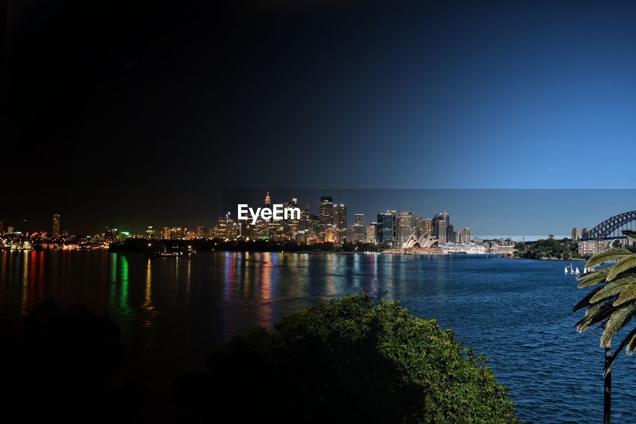 Distant view of illuminated city by sydney harbour at night