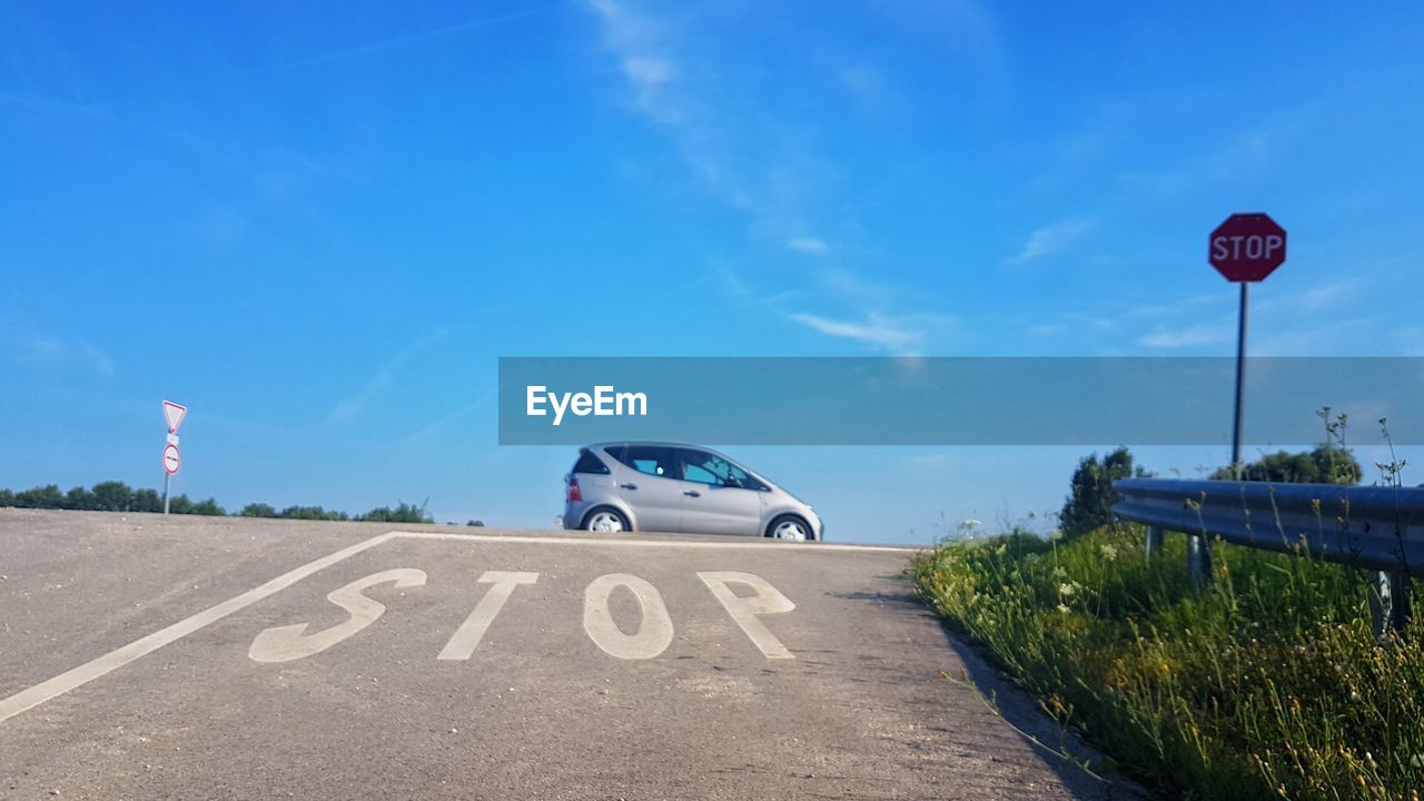 Car by stop sign on road against blue sky