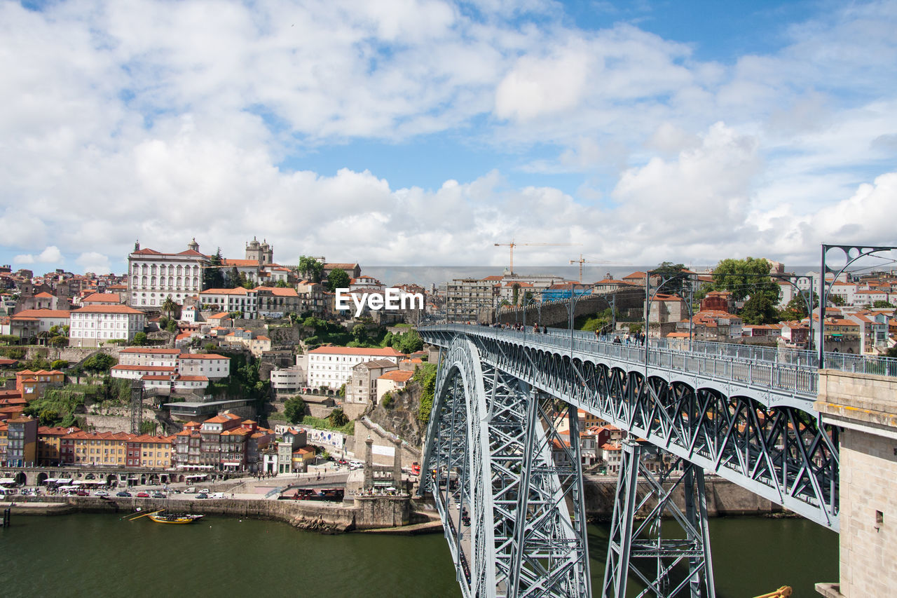 Dom luis i bridge over douro river by townscape against cloudy sky