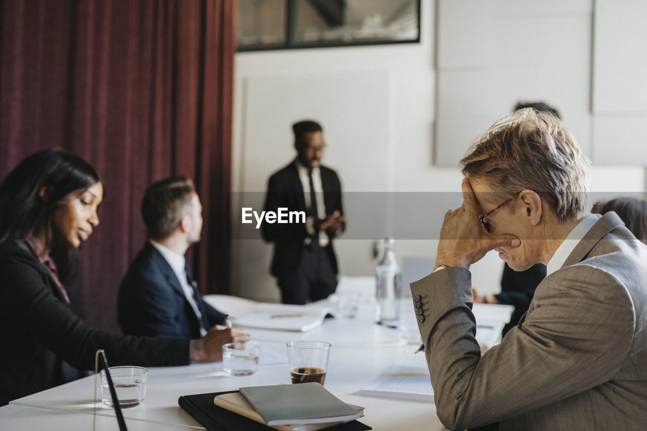 Side view of businessman with head in hand during meeting with colleagues in board room at office