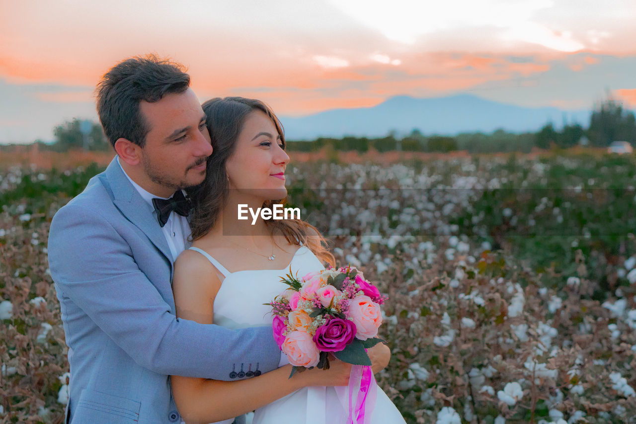 Smiling bride and groom with bouquet romancing on field