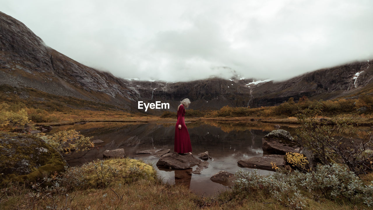 Woman standing on rock amidst mountains against sky