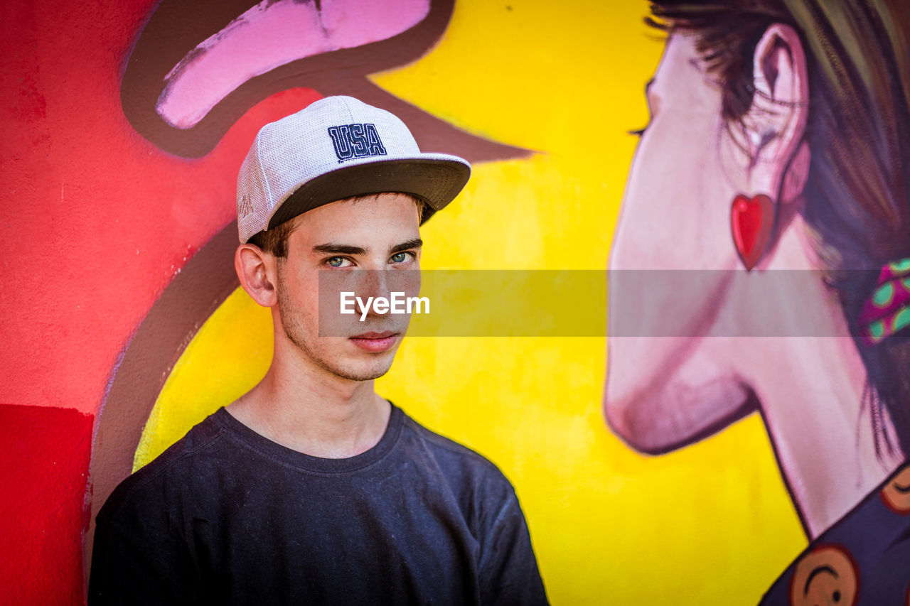 PORTRAIT OF YOUNG MAN AGAINST YELLOW WALL AGAINST GRAFFITI