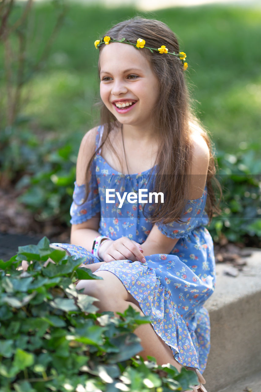 Smiling girl sitting against plants in park