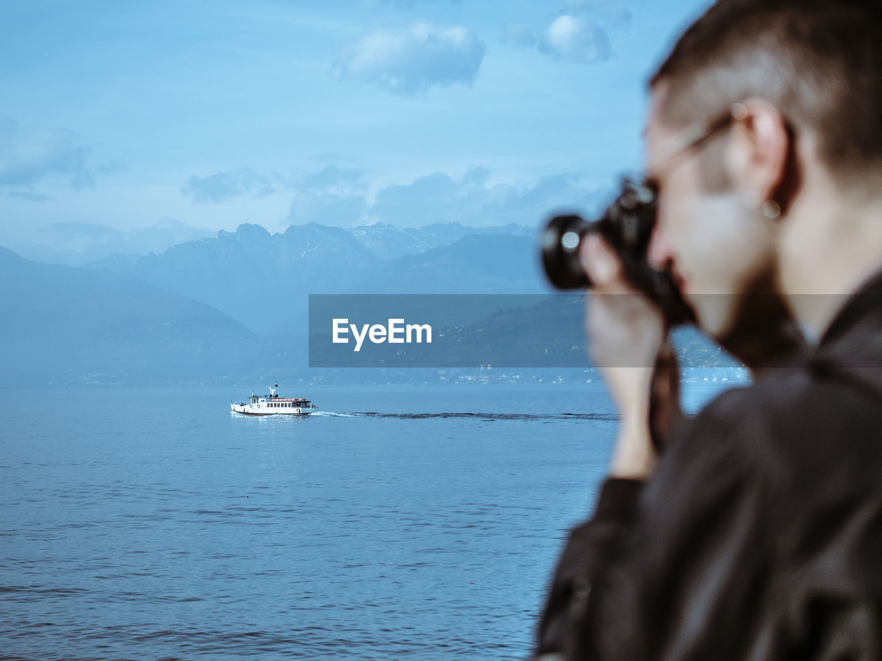 Side view of man photographing sea against blue sky