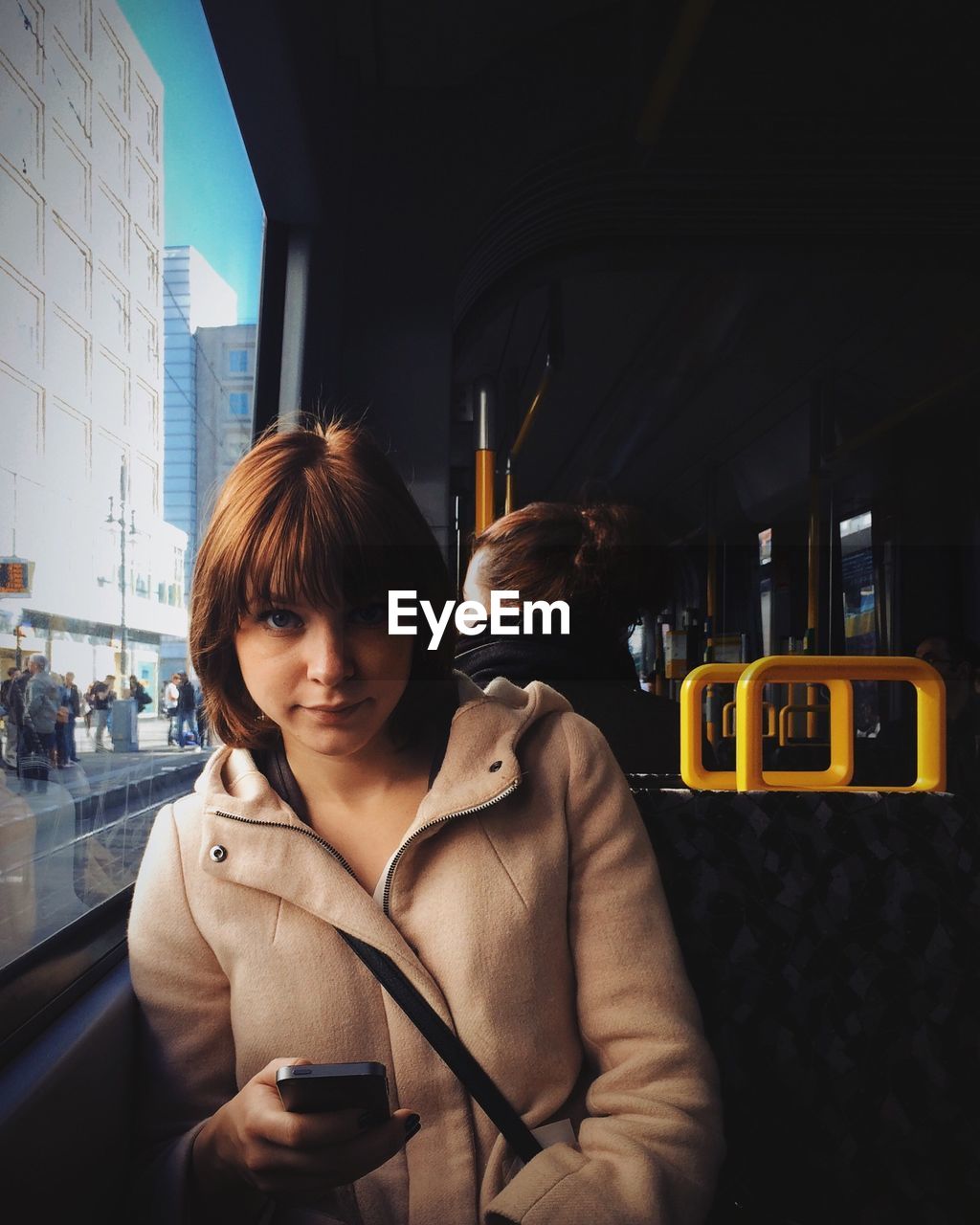 Portrait of young woman using mobile phone while traveling in tram