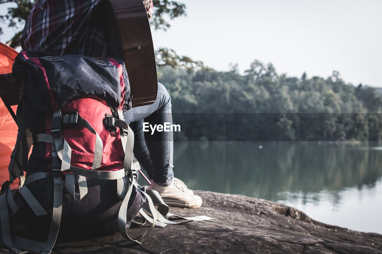 Rear view of man sitting on rock by lake against sky