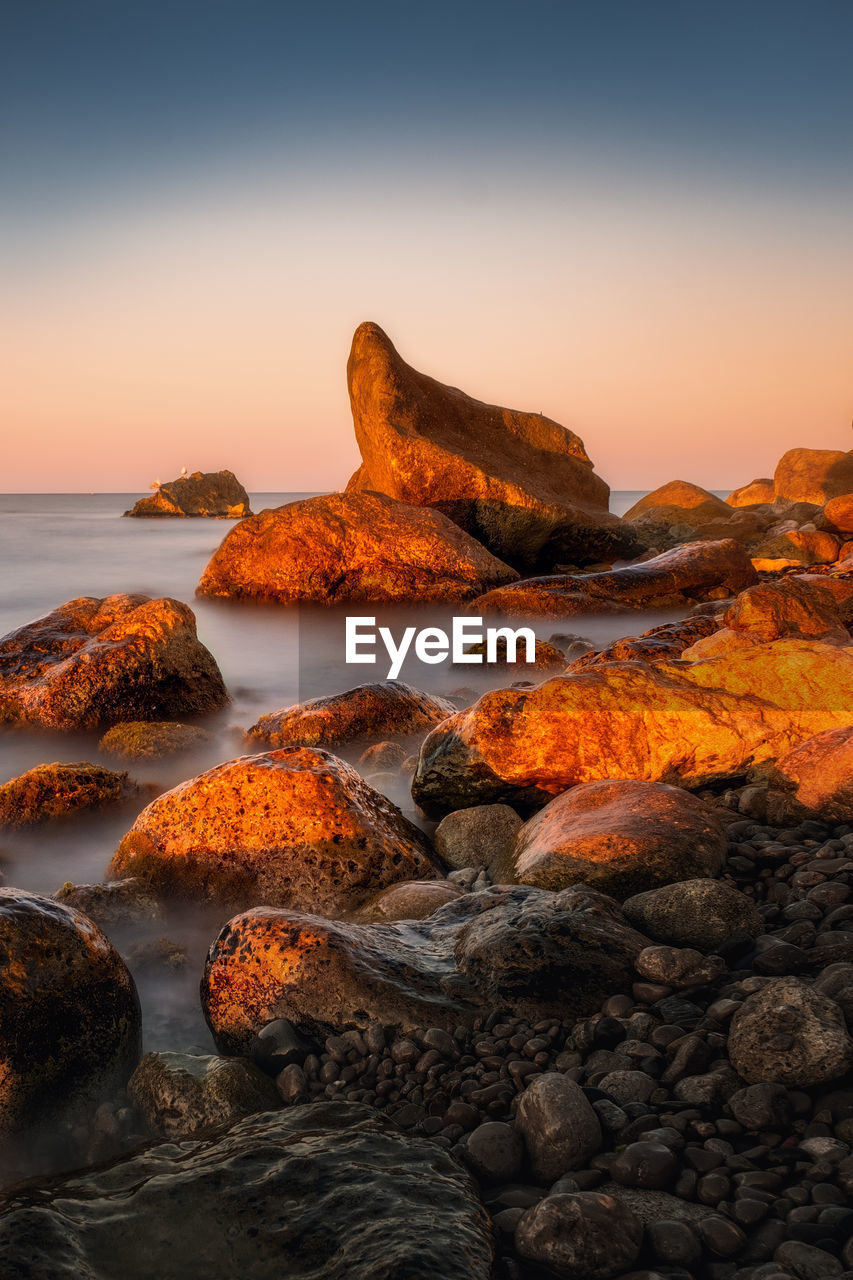 Rocks on sea shore against sky during sunset