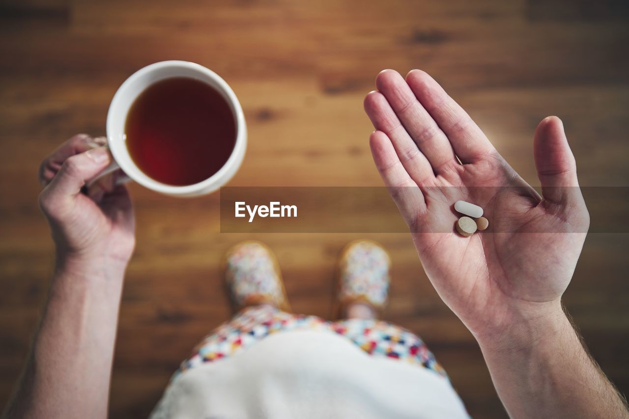 Sick man in nightwear is taking pills and cup of  tea. 