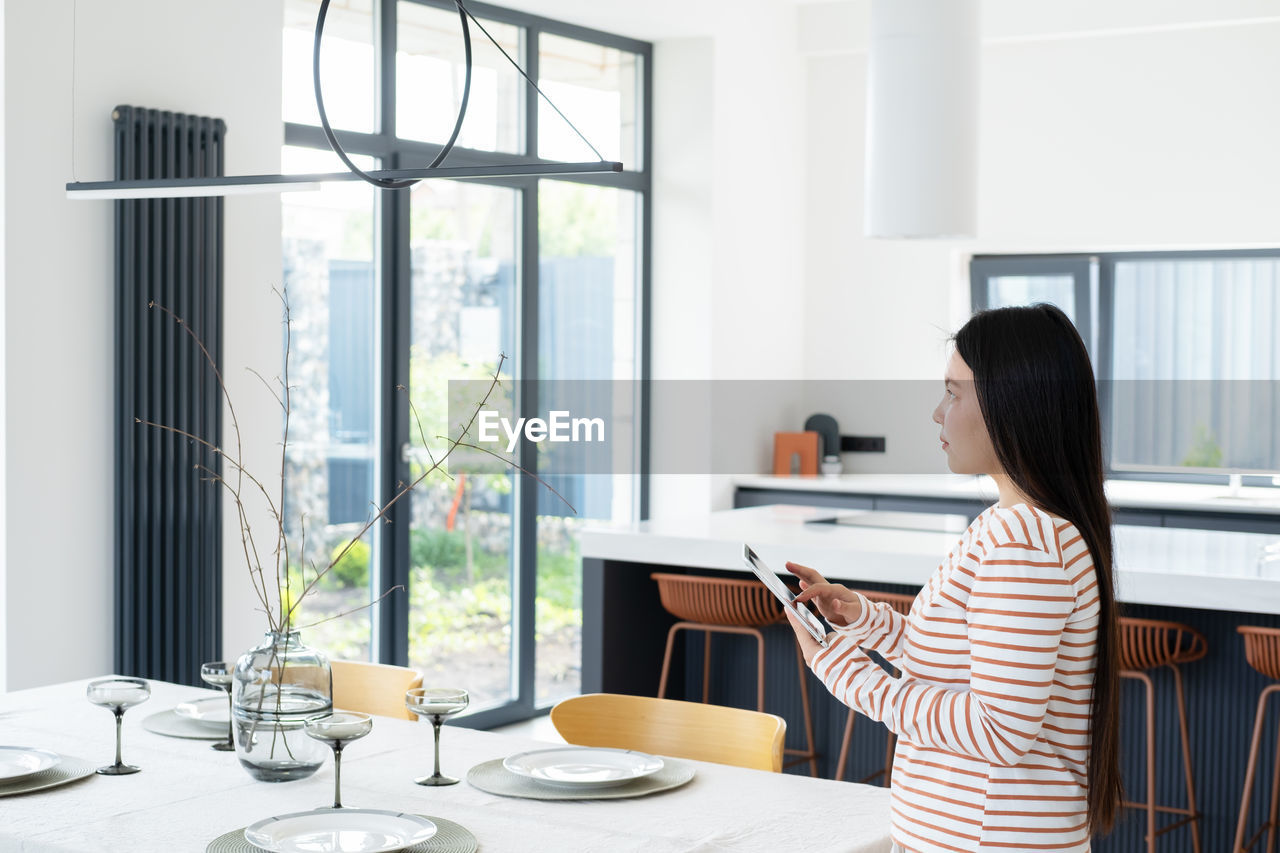 Woman with digital tablet controlling light over dining table modern apartment