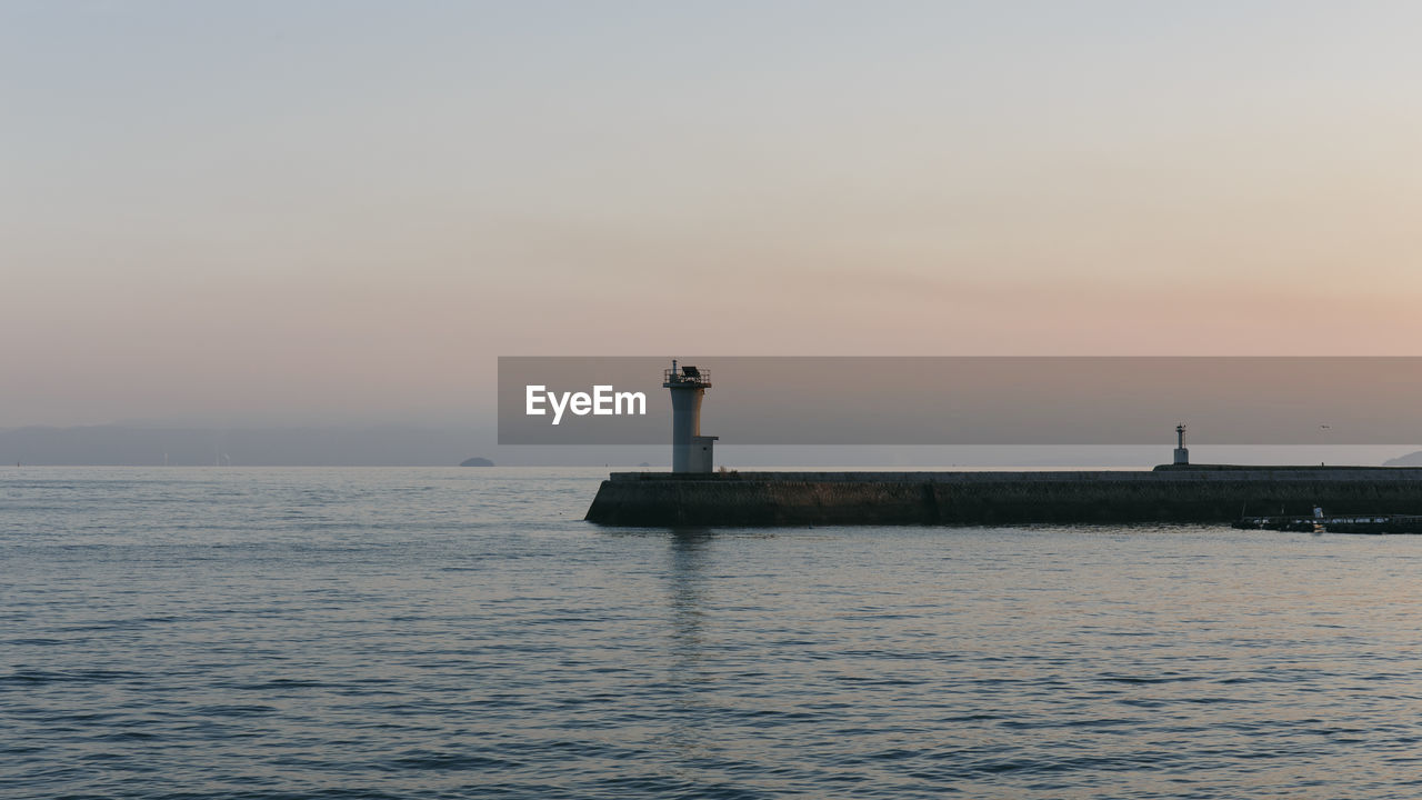 Lighthouse by sea against sky during sunset