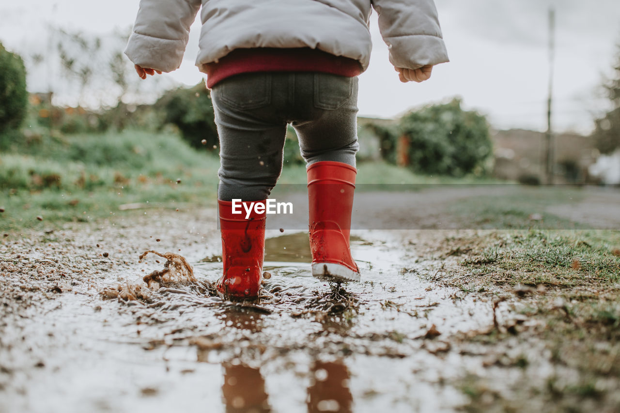 Low section of baby girl walking on puddle during rainy season