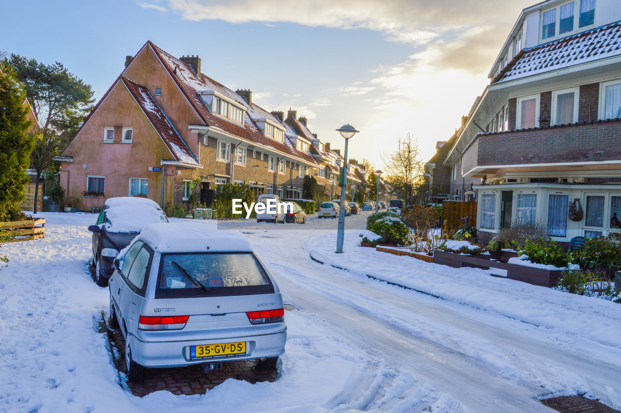 CARS ON ROAD BY HOUSES AGAINST SKY