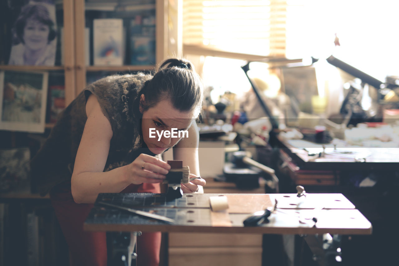 Girl master processes the metal copper plate on the workbench in the home workshop, soft focus 