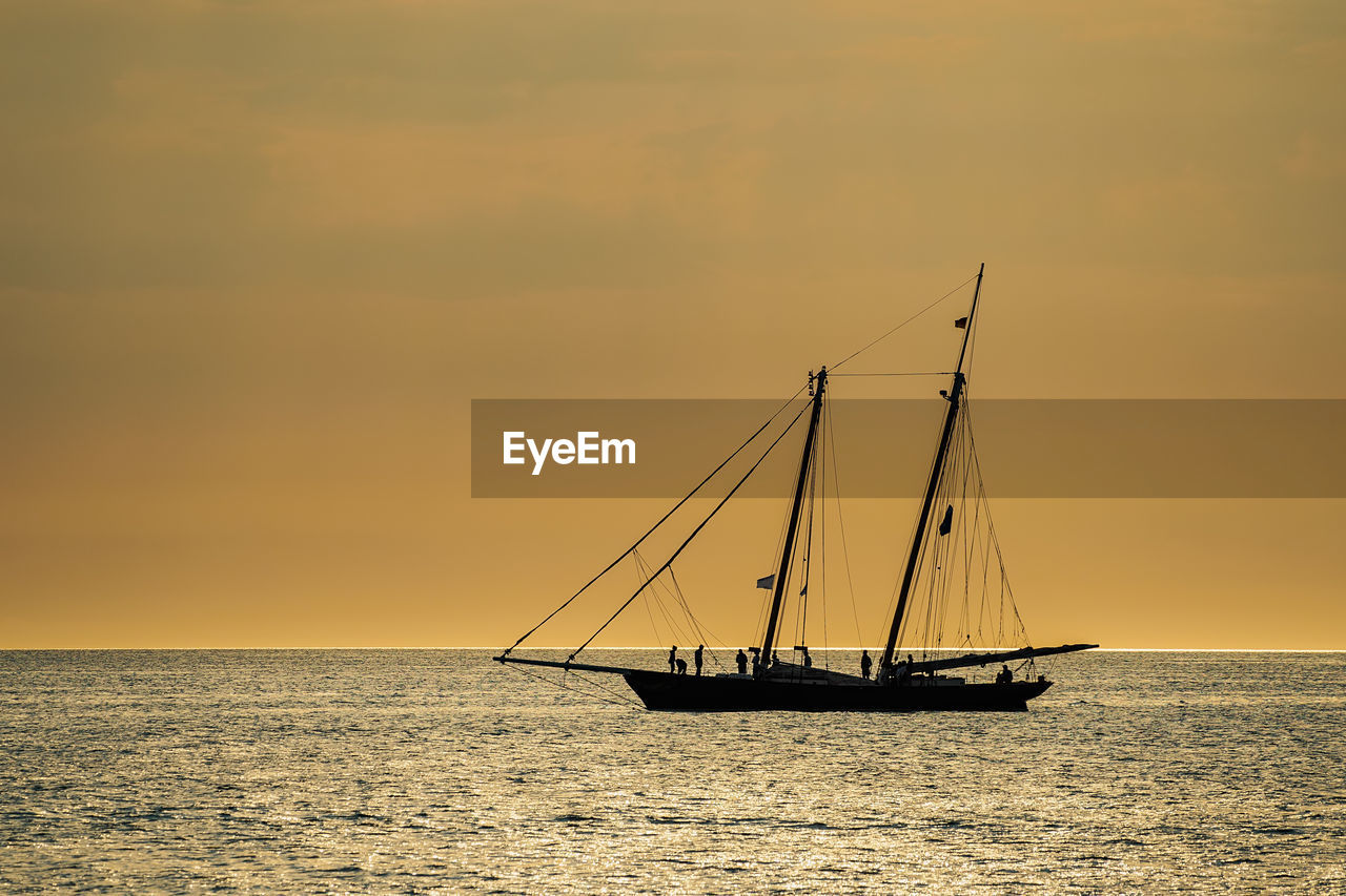 SILHOUETTE SAILBOAT SAILING ON SEA AGAINST SKY AT SUNSET