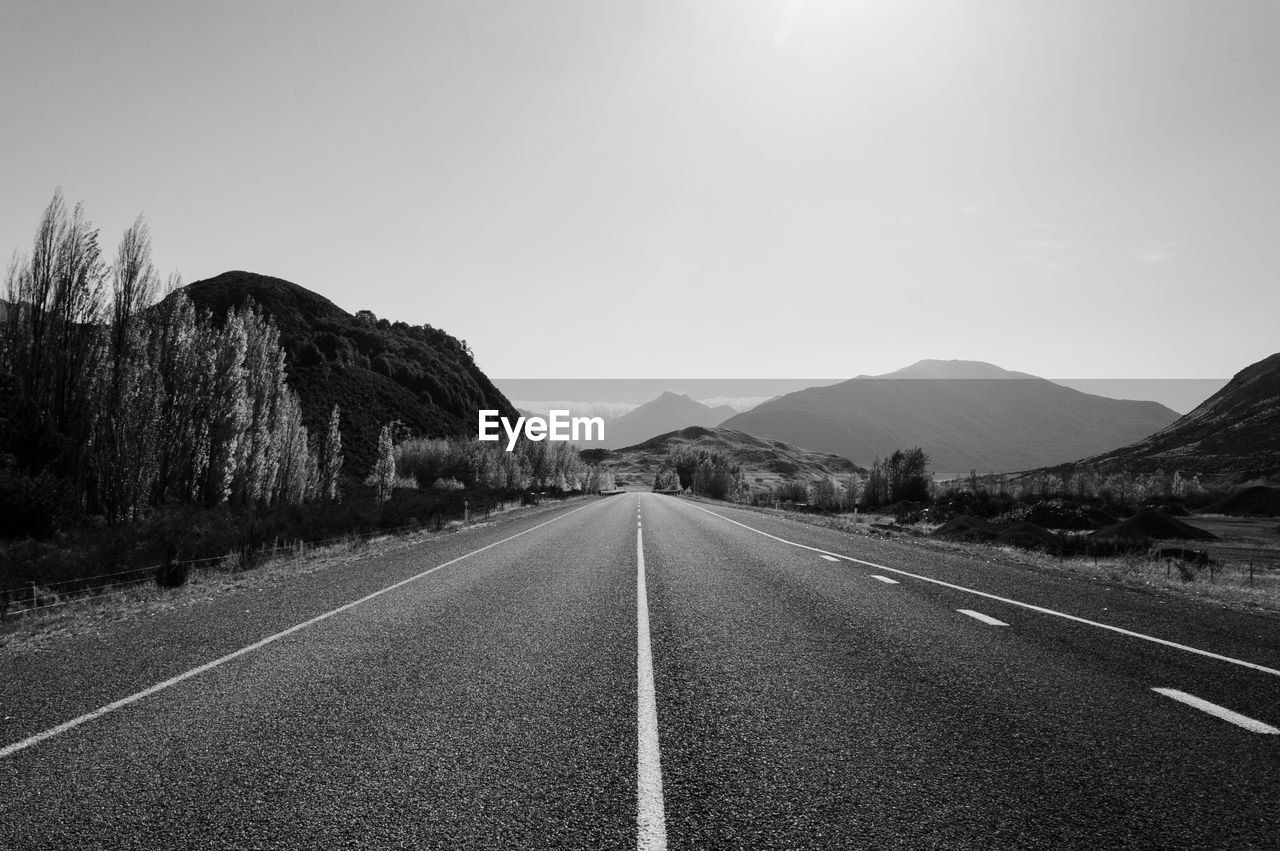 Empty road by mountains against clear sky