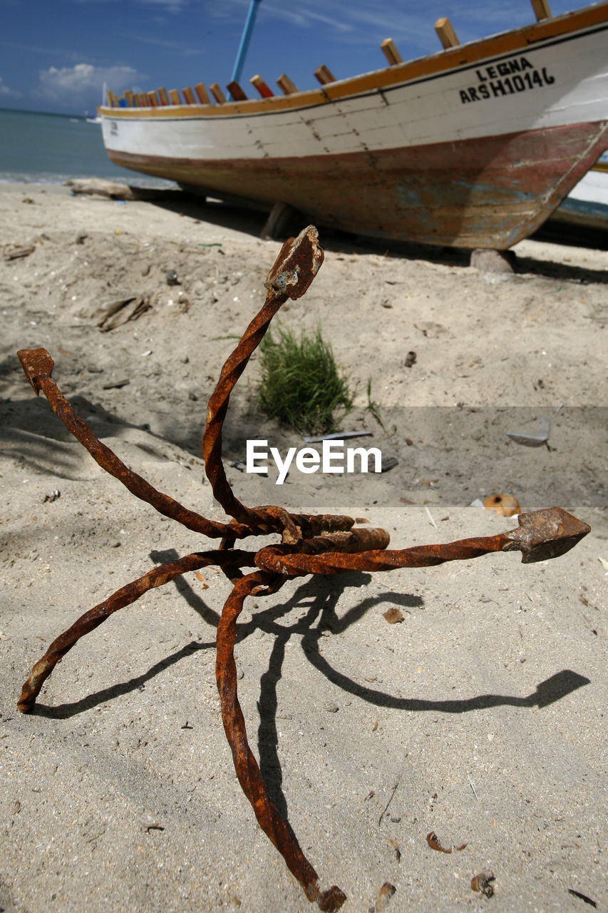 Rusty anchor by moored boat at beach against sky