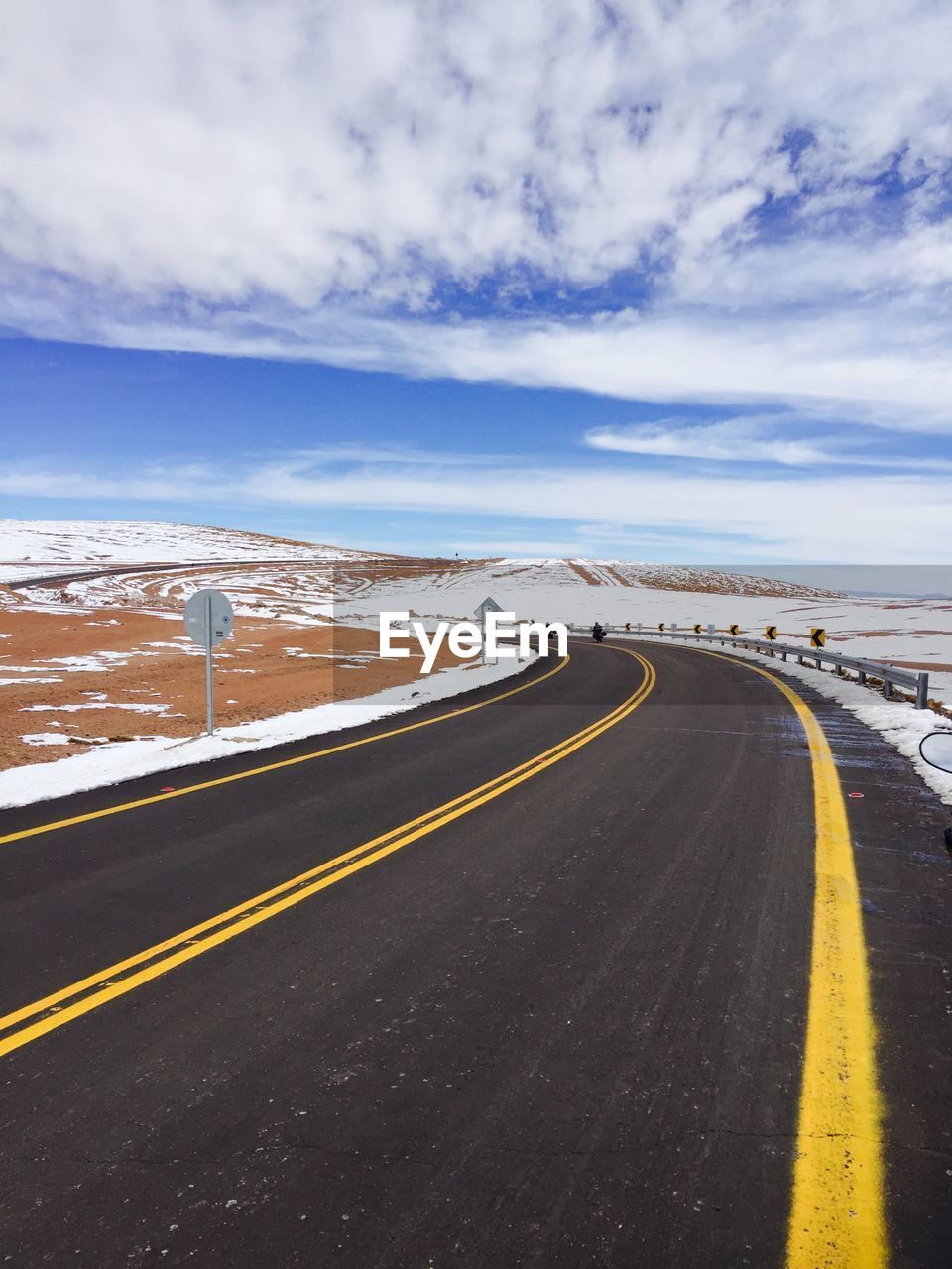 Empty road amidst snow covered landscape against cloudy sky