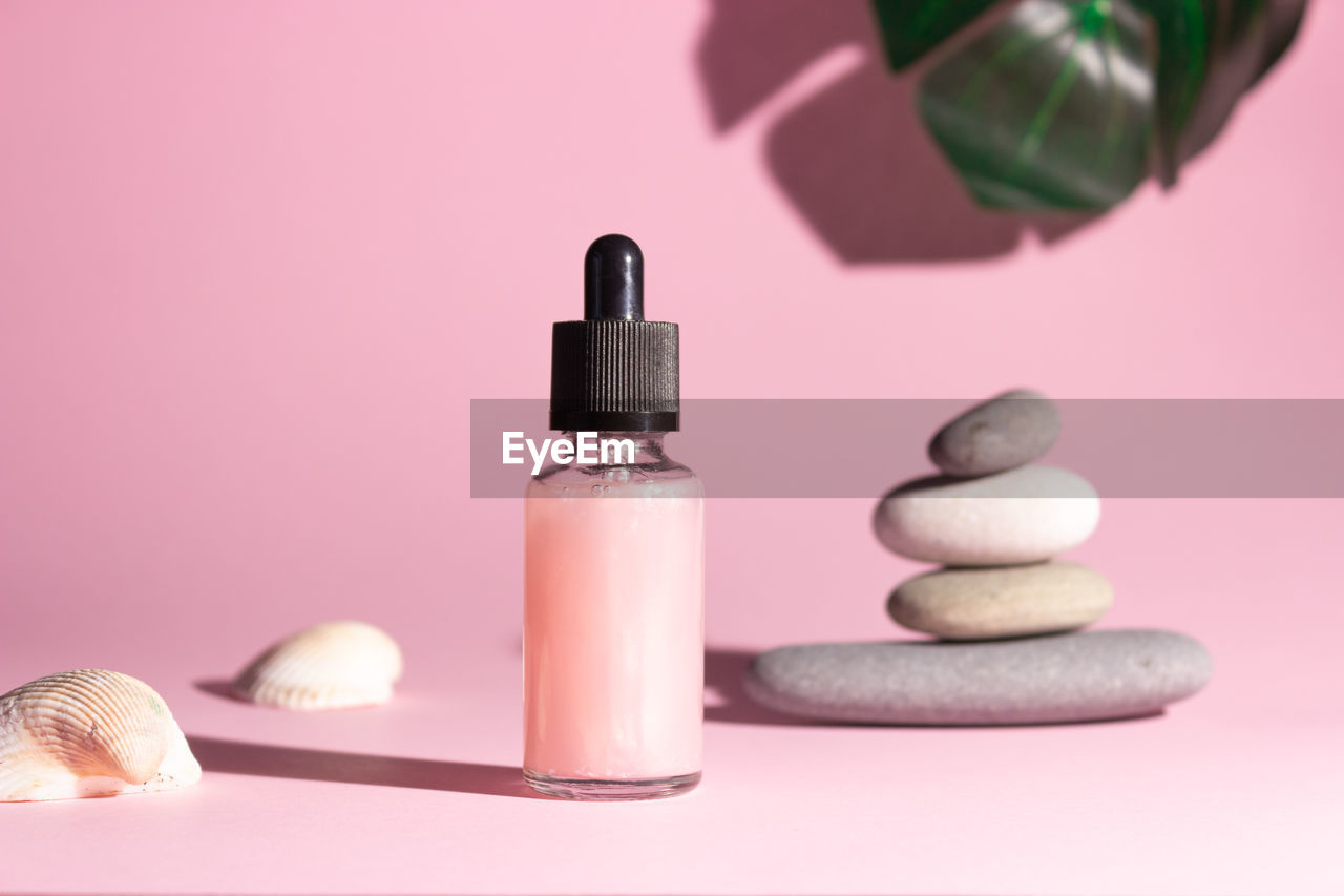 Cosmetic product in a glass bottle with a pipette on a pink background. smooth stones nearby.